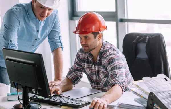 Ingénieurs technico-commerciaux en réunion devant un ordinateur, portant des casques de chantier