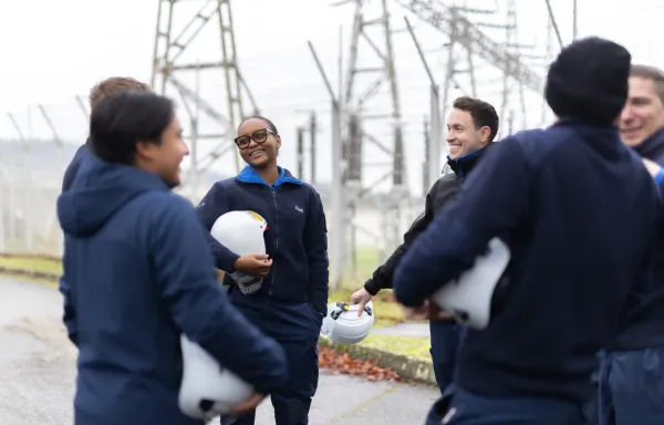 Groupe de jeunes techniciens souriants en extérieur, tenant des casques de sécurité