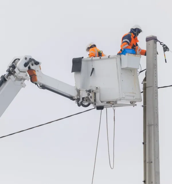 Deux techniciens travaillant en hauteur dans une nacelle sur un poteau électrique