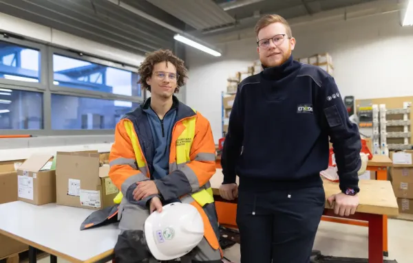 Deux techniciens en tenue de travail posant dans un atelier, casque de chantier à la main