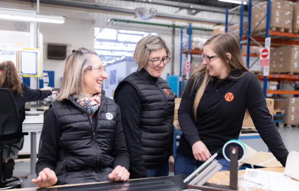 Trois collaboratrices souriantes échangeant dans un entrepôt industriel