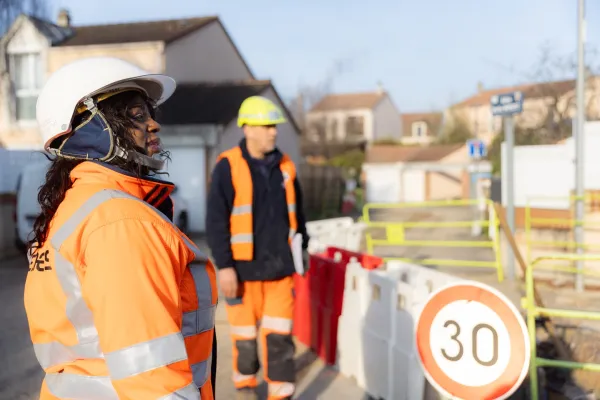 Technicienne sur un chantier, en tenue de sécurité orange et casque blanc