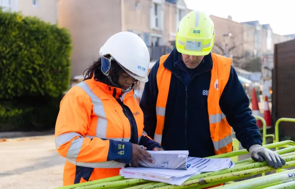 Deux techniciens consultant des plans sur un chantier, portant casques et gilets de sécurité
