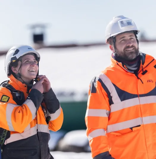 Deux techniciens en tenue de sécurité souriants sur un chantier enneigé