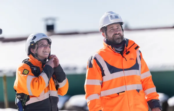 Deux monteurs de réseaux électriques en tenue de sécurité, souriants sur un chantier enneigé