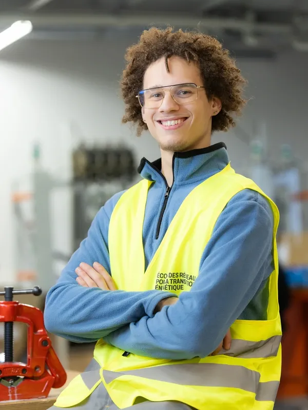 Guillaume, technicien souriant en gilet de sécurité, bras croisés dans un atelier