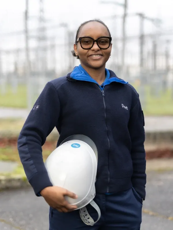 Technicienne de maintenance souriante en extérieur, tenant un casque de sécurité