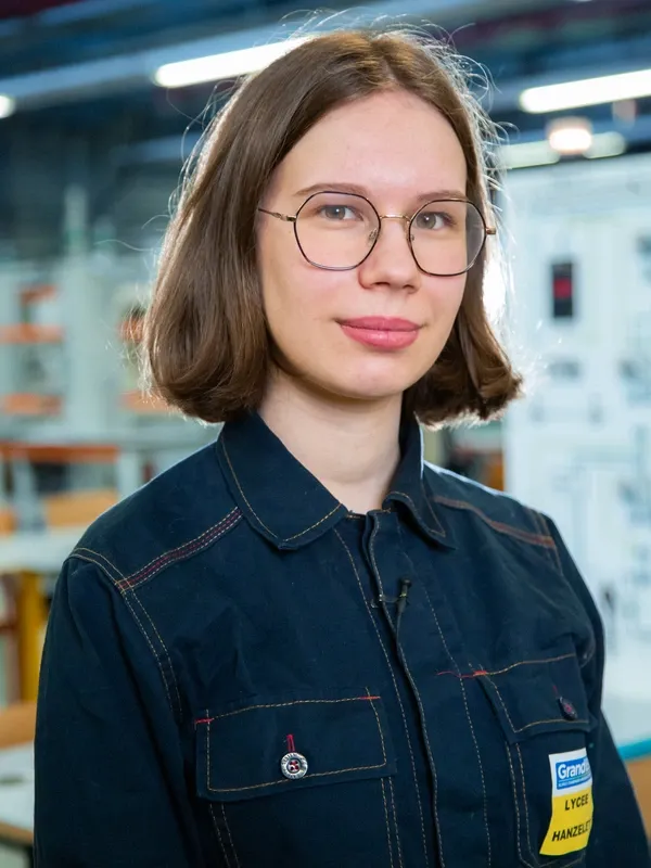 Portrait de Maëlle en tenue de travail dans un atelier technique, portant des lunettes et un badge du lycée