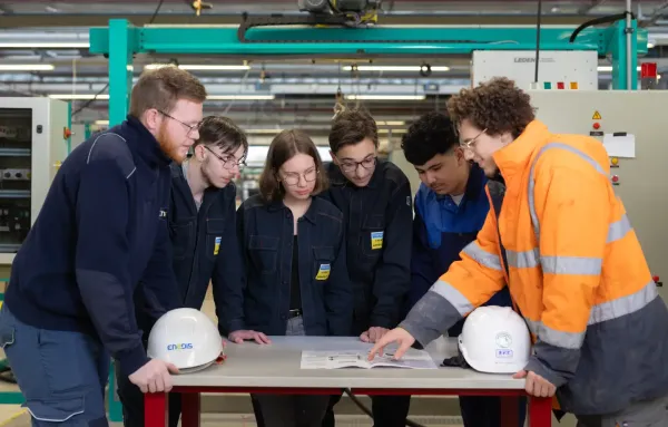 Groupe d'étudiants en formation technique autour d'une table avec plans, dans un atelier
